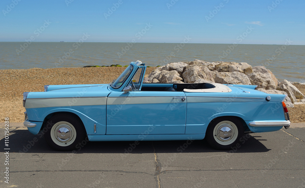 Classic light Blue Triumph Herald open top motor car parked on seafront promenade.