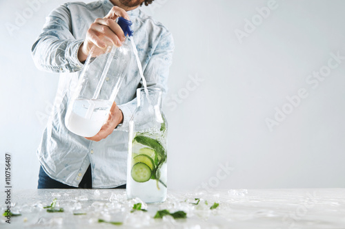 Photos Bartender pours sparkling water in vintage bottle with ice, cucumber and mint fr