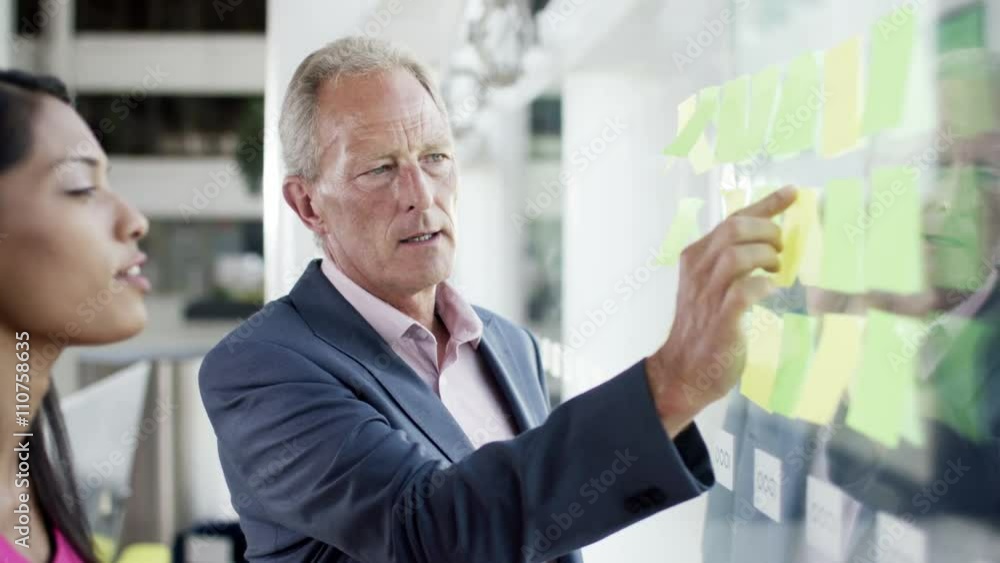 Attractive business man and woman brainstorming for ideas with sticky notes Attractive business man and woman brainstorming for ideas with sticky notes