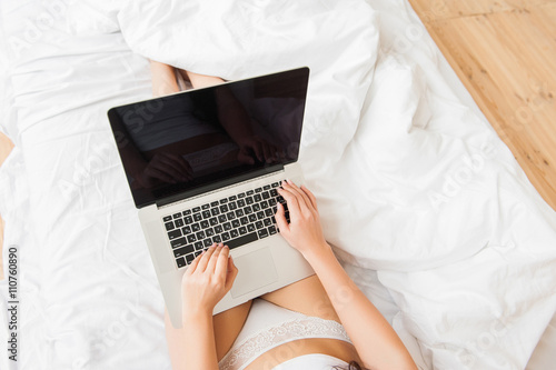 Young woman at home in bed and checking laptop, topview