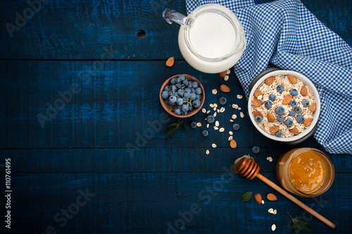 A healthy breakfast on a dark blue wooden background: Oatmeal, milk, blueberries, honey and almonds. Rustic style.
