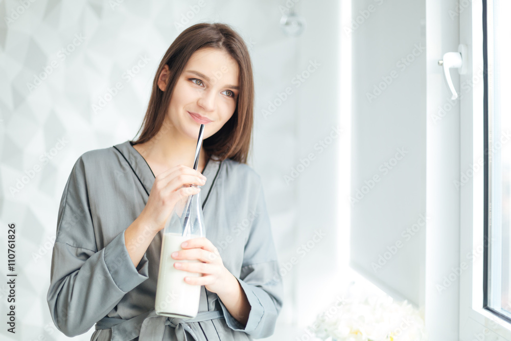 Happy attractive young woman in grey bathrobe drinking milk Happy attractive young woman in grey bathrobe drinking milk