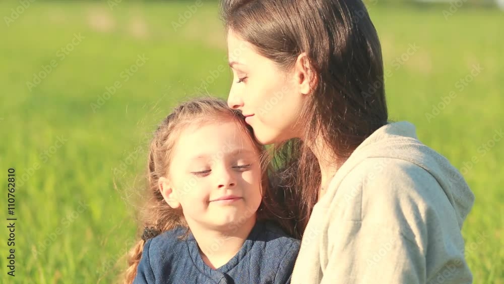 Happy emotional daughter hugging and kissing with love her young smiling mother on summer background Happy emotional daughter hugging and kissing with love her young smiling mother on summer background