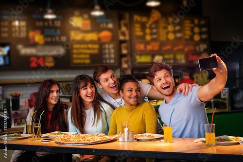 Cheerful multiracial friends taking selfie in pizzeria.