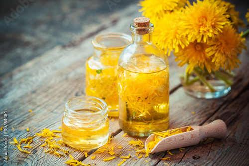 Obraz na płótnie Bottles of dandelion tincture or oil, flower bunch, wooden scoop