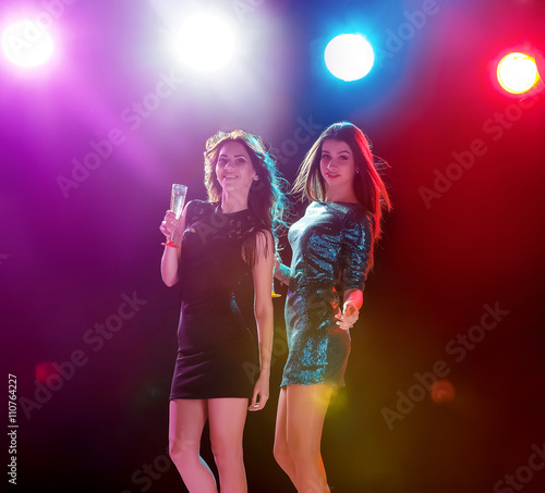 Two beautiful girls dancing at the party drinking champagne