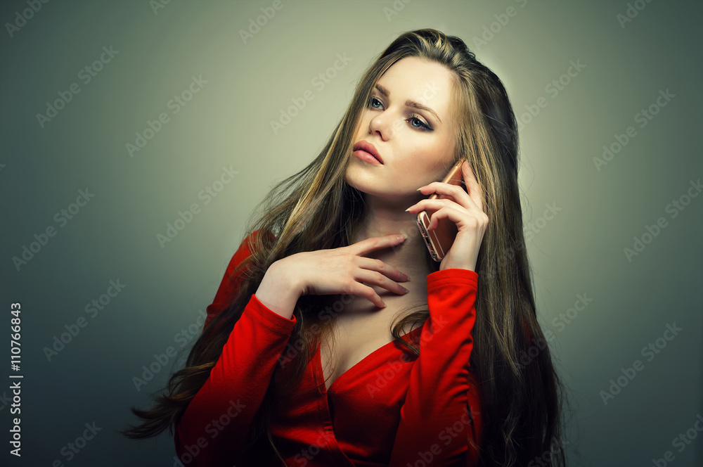 Beautiful young woman in red dress with perfect cute face talking on smartphone. Studio fashion portrait. Beautiful young woman in red dress with perfect cute face talking on smartphone. Studio fashion portrait.