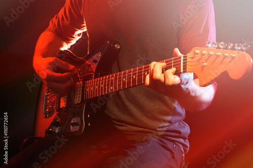 Young man playing on electric guitar on dark background with light effect