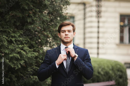 Young stylish businessman adjusting his suit, neck tie