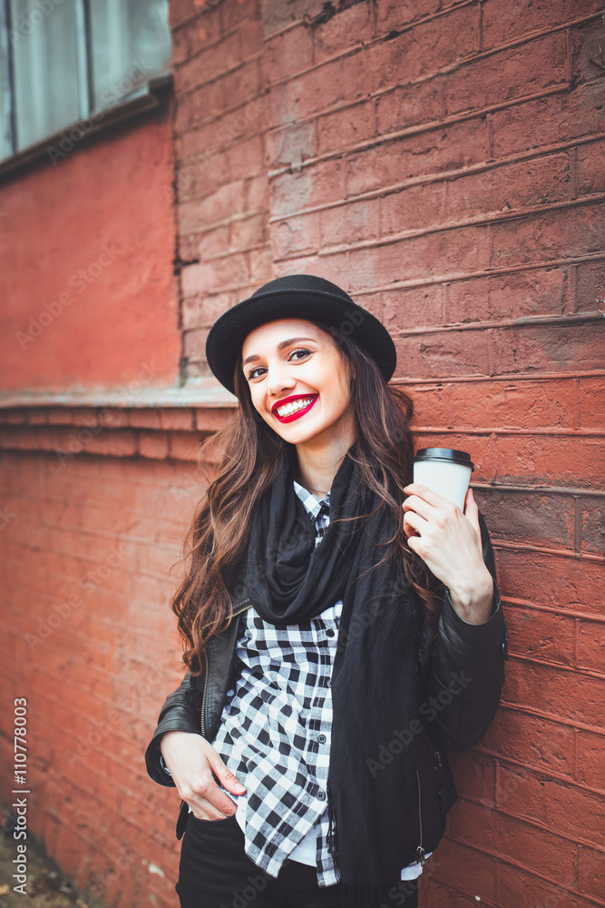Trendy woman in hat with drink outdoor. Young woman  in the street and holding cup of coffee