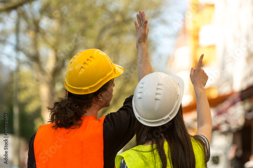 Back turned architects, a boy and a girl both with long hair, pointing at something at construction site