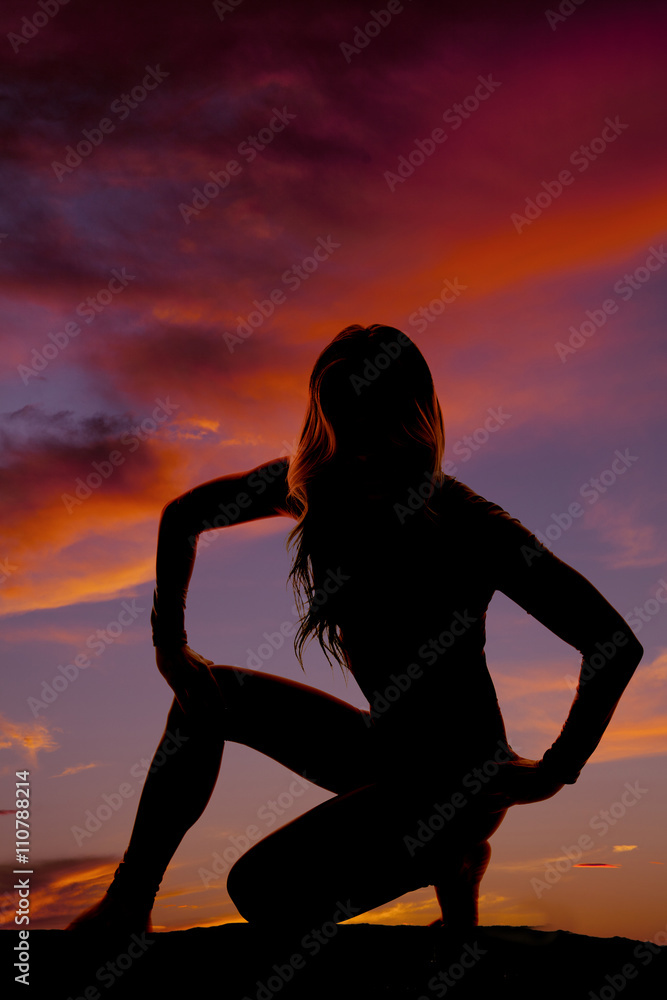 silhouette of a woman down with hand on one knee in sunset