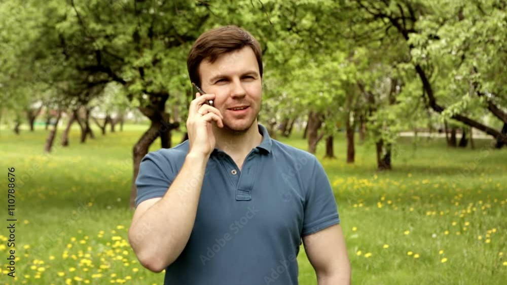 Handsome hipster man in t-shirt talking on phone with friend on a sunny day in park Handsome hipster man in t-shirt talking on phone with friend on a sunny day in park