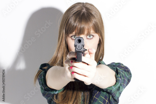 Blonde woman holding a pistol, aiming to camera, aggressive, over a white wall.
