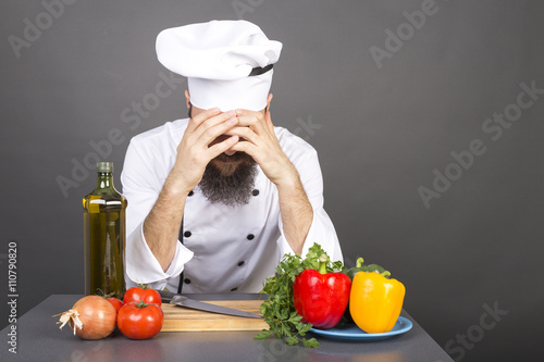 Young chef covers face with hands, having problems,