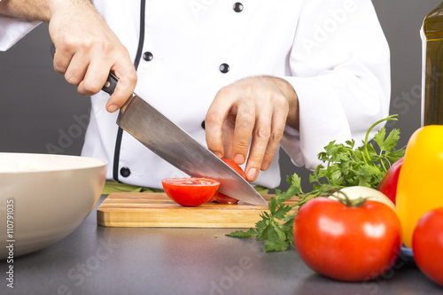 Chef's hands cutting red fresh tomato