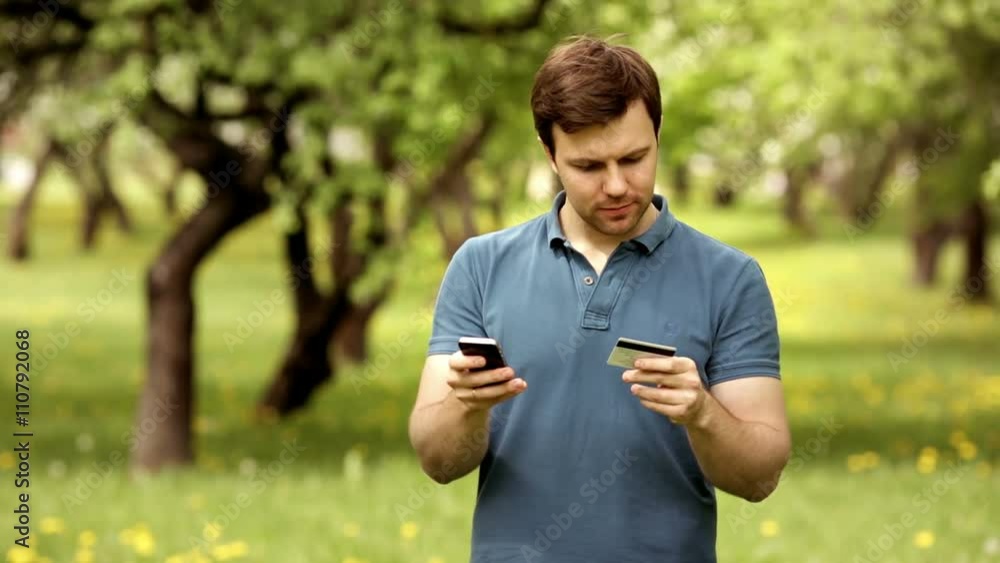 Man with credit card during shopping through internet using smart phone in park with copyspace Man with credit card during shopping through internet using smart phone in park with copyspace