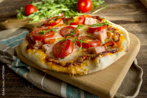 homemade pizza with ham , tomato and arugula on a wooden board.