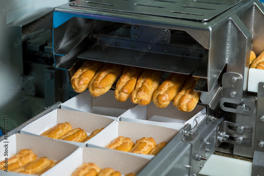 Boxes with eclairs on conveyor. Machine puts eclairs into boxes. Even portions of dessert. Pastry with delicious filling. Boxes with eclairs on conveyor. Machine puts eclairs into boxes. Even portions of dessert. Pastry with delicious filling.