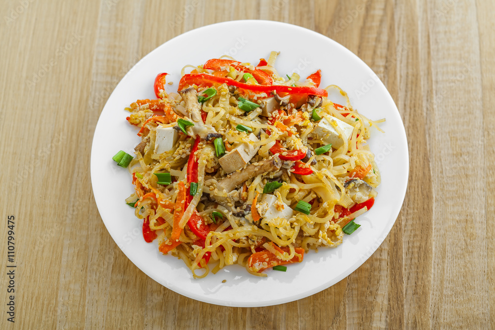 Plate of stirred rice noodles with tofu, vegetables and shiitake on a table. Traditional Asian cuisine meal. Top view.