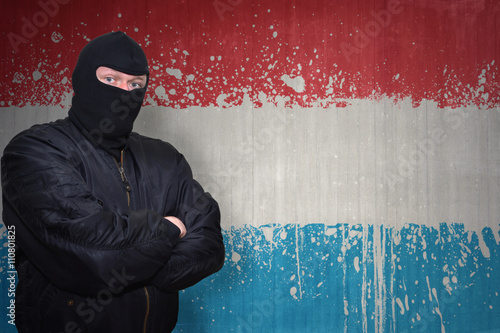 dangerous man in a mask standing near a wall with painted national flag of luxembourg