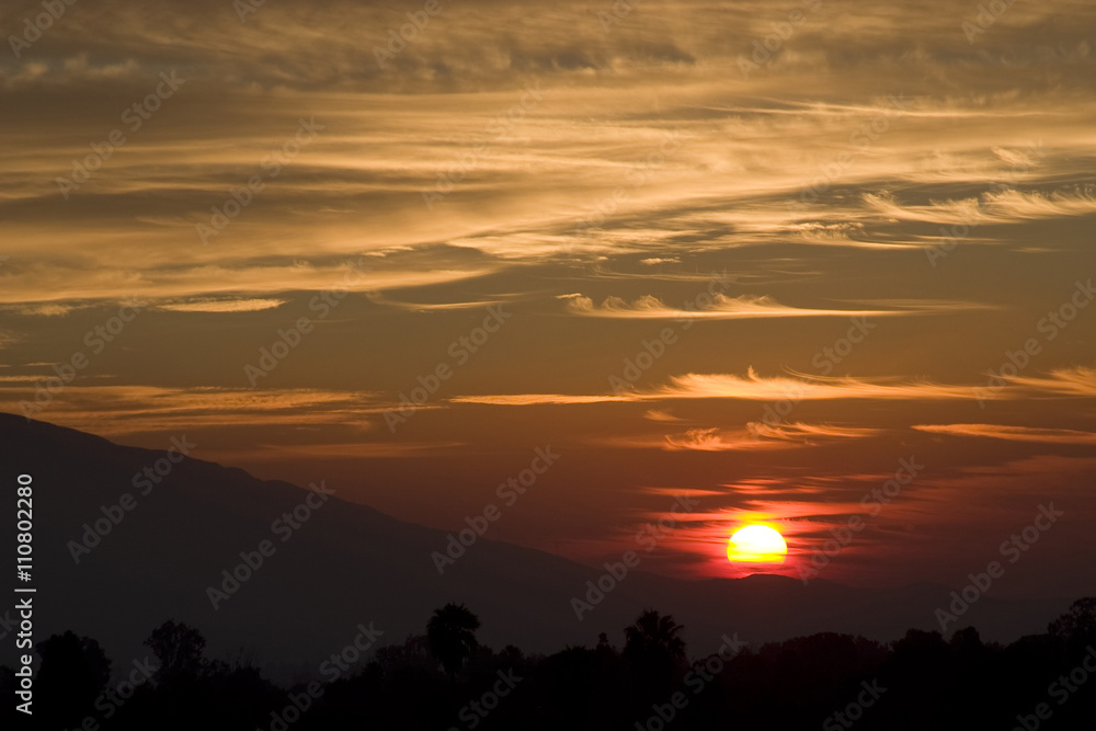 Crimson sunset, sun setting behind crest of mountain hill