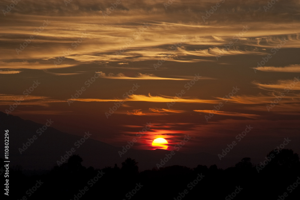 Crimson sunset, sun setting behind crest of mountain hill Crimson sunset, sun setting behind crest of mountain hill