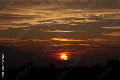 Crimson sunset, sun setting behind crest of mountain hill