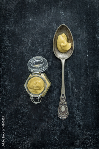 Old vintage spoon and mustard jar on black chalkboard - top view