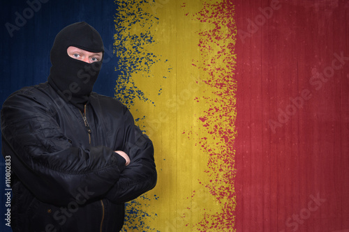 dangerous man in a mask standing near a wall with painted national flag of romania
