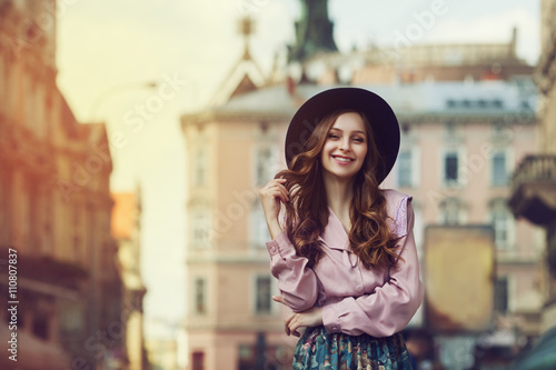 Outdoor portrait of young beautiful fashionable smiling lady posing on old street. street. Model wearing stylish hat & clothes. Sunny day. Female fashion. City lifestyle. Toned style instagram filters