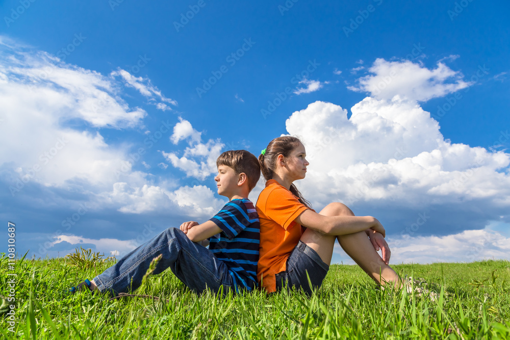 Two kids sitting back-to-back on grass Two kids sitting back-to-back on grass