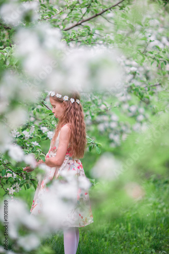 Little cute girl in blooming cherry garden outdoors