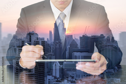 Double exposure of business man working with tablet, city, urban and sunset as communication and technology concept.