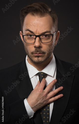 Portrait of businessman adjusting his tie in studio. Young man in glasses looking at camera with serious face. No emotions.