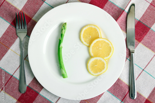 delicious asparagus with sliced lemon on a round plate and Cutlery on a napkin. Top view