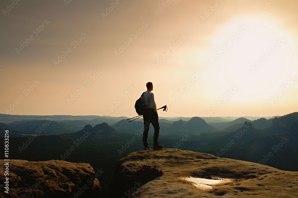 Tall ginger hair hiker in grey t-shirt and dark trekking trousers on cliff. Man with tourist poles in hand and sporty backpack above valley. Tall ginger hair hiker in grey t-shirt and dark trekking trousers on cliff. Man with tourist poles in hand and sporty backpack above valley.