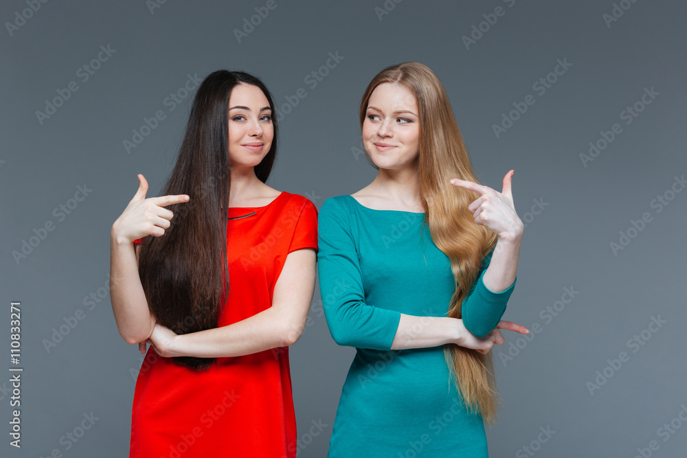 Two happy girlfriends pointing fingers at each other Two happy girlfriends pointing fingers at each other