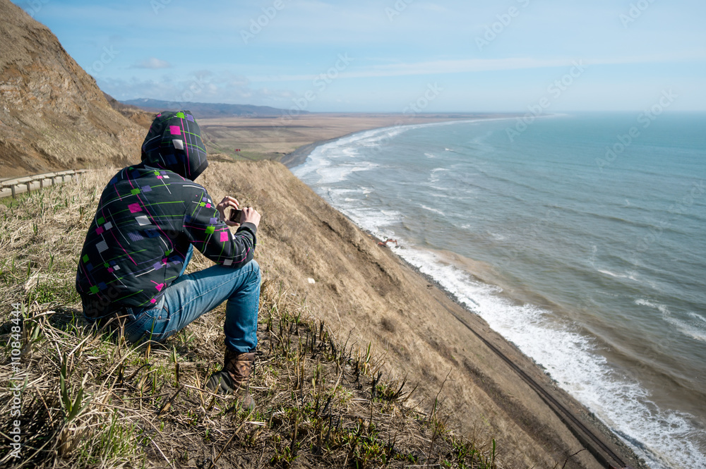 Fototapeta premium Man sitting on a hill and looking at the sea