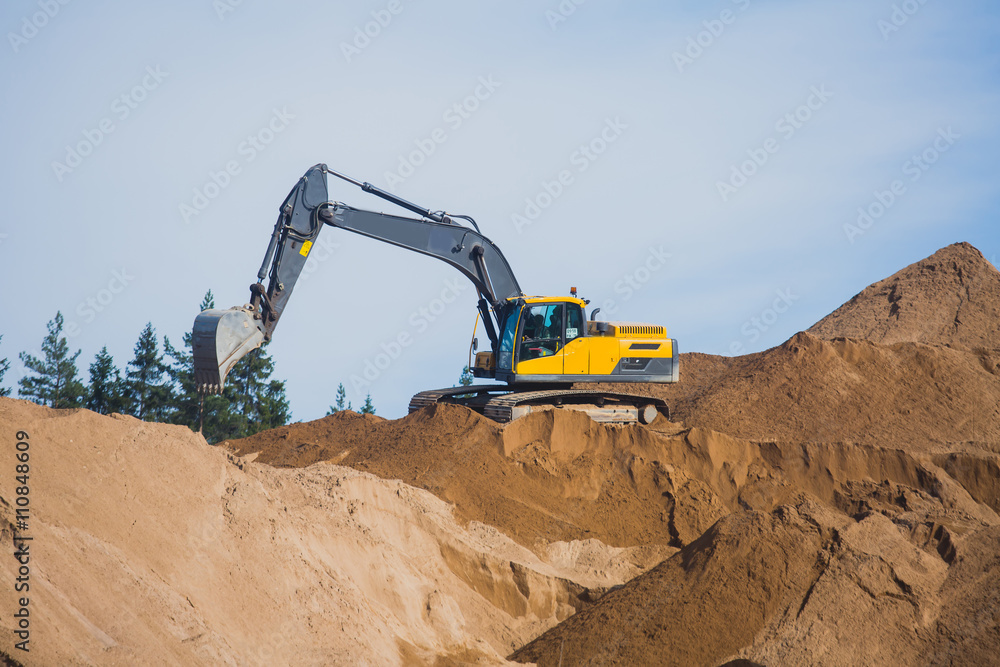 Yellow heavy excavator and bulldozer excavating sand and working during road works, unloading sand and road metal during construction of the new road