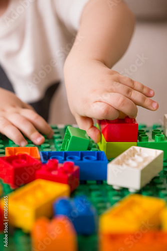 Close up of child s hands playing with colorful plastic bricks at the table. Toddler having fun and building out of bright constructor bricks. Early learning.  stripe background. Developing toys