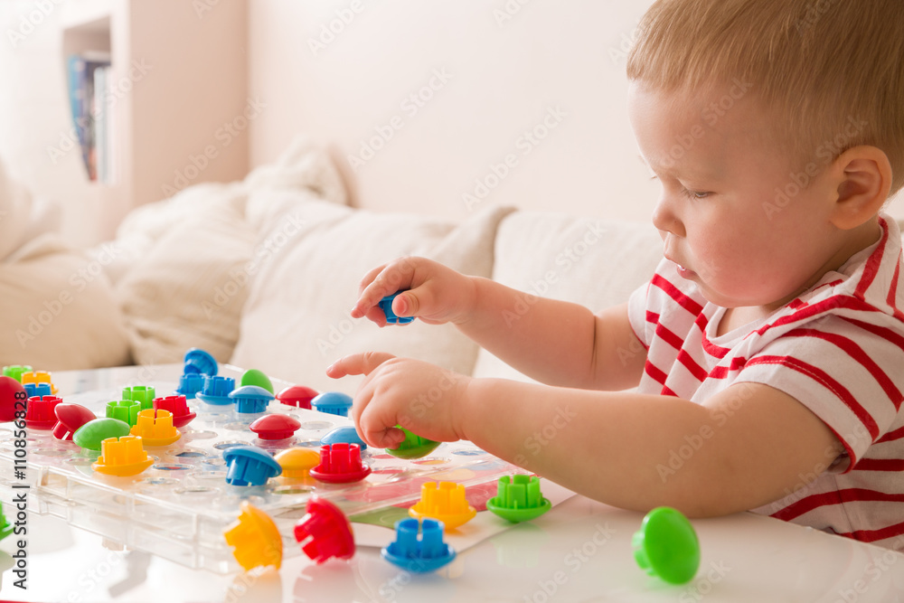 Closeup of child's hand taking bright mosaic parts. Playing and learning colors at home. Toddler boy in a striped shirt playing with colorful constructor details. Activities with children Closeup of child's hand taking bright mosaic parts. Playing and learning colors at home. Toddler boy in a striped shirt playing with colorful constructor details. Activities with children