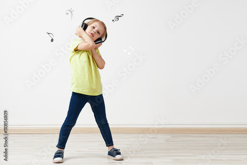 Portrait of pretty Caucasian girl wearing headphones over empty wall background with music notes and copy space. 