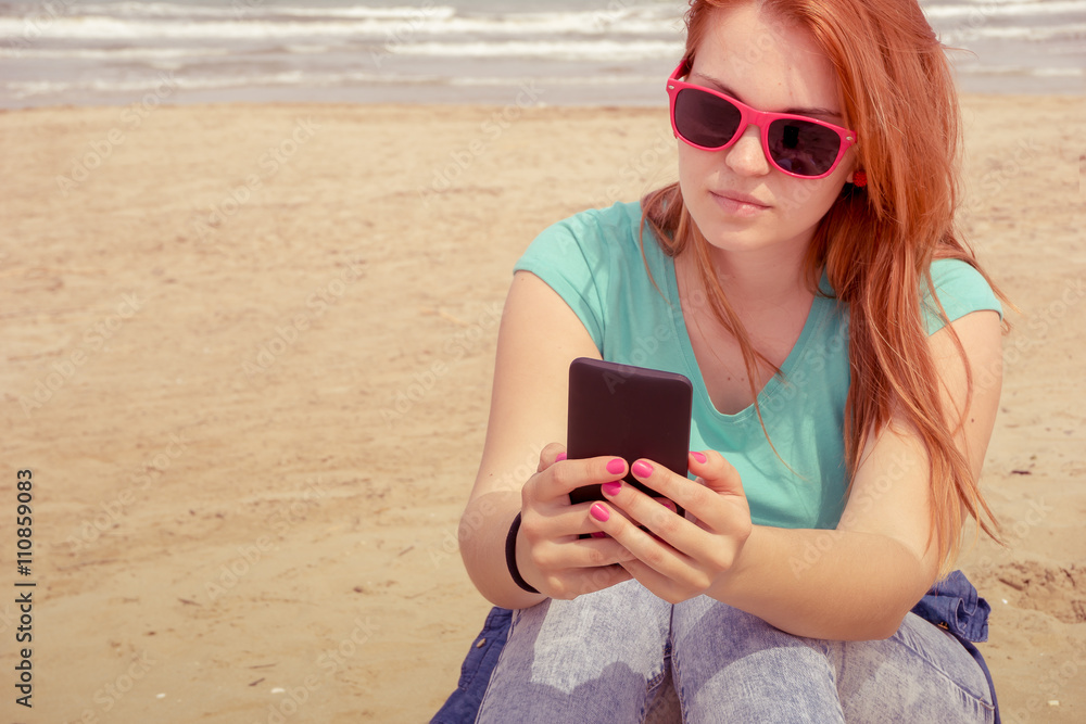 beautiful woman with smartphone and sunglasses sitting on a sunny  beach