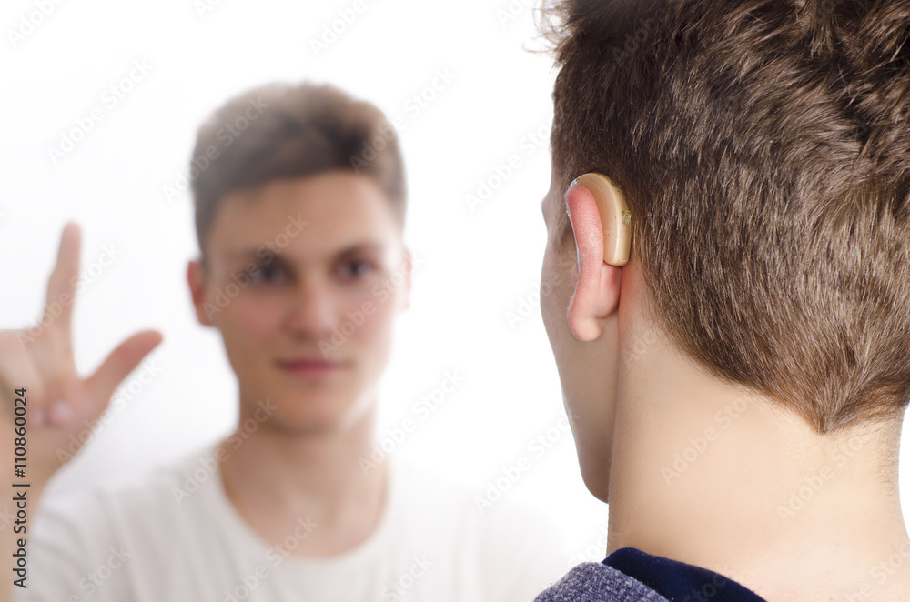 Two deaf-mute teenagers communicating using sign language, selective focus on hearing aid Two deaf-mute teenagers communicating using sign language, selective focus on hearing aid