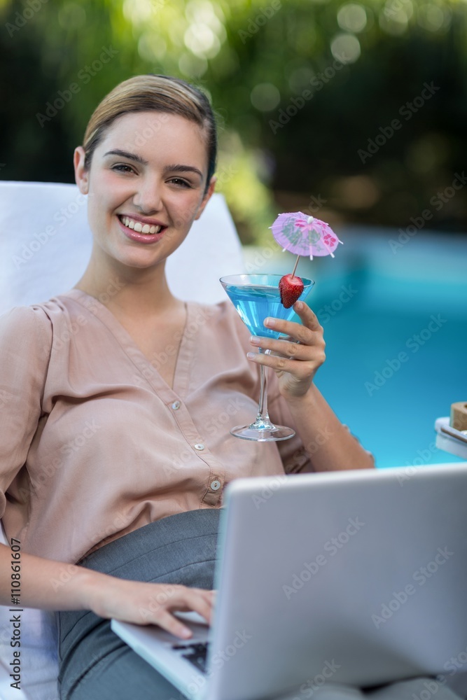 Businesswoman holding glass of martini while using laptop Businesswoman holding glass of martini while using laptop