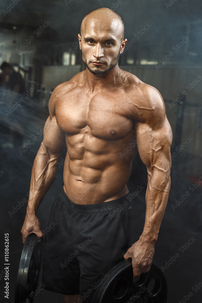 Fototapeta premium very power athletic guy standing in gym with dumbbells and lokking at camera