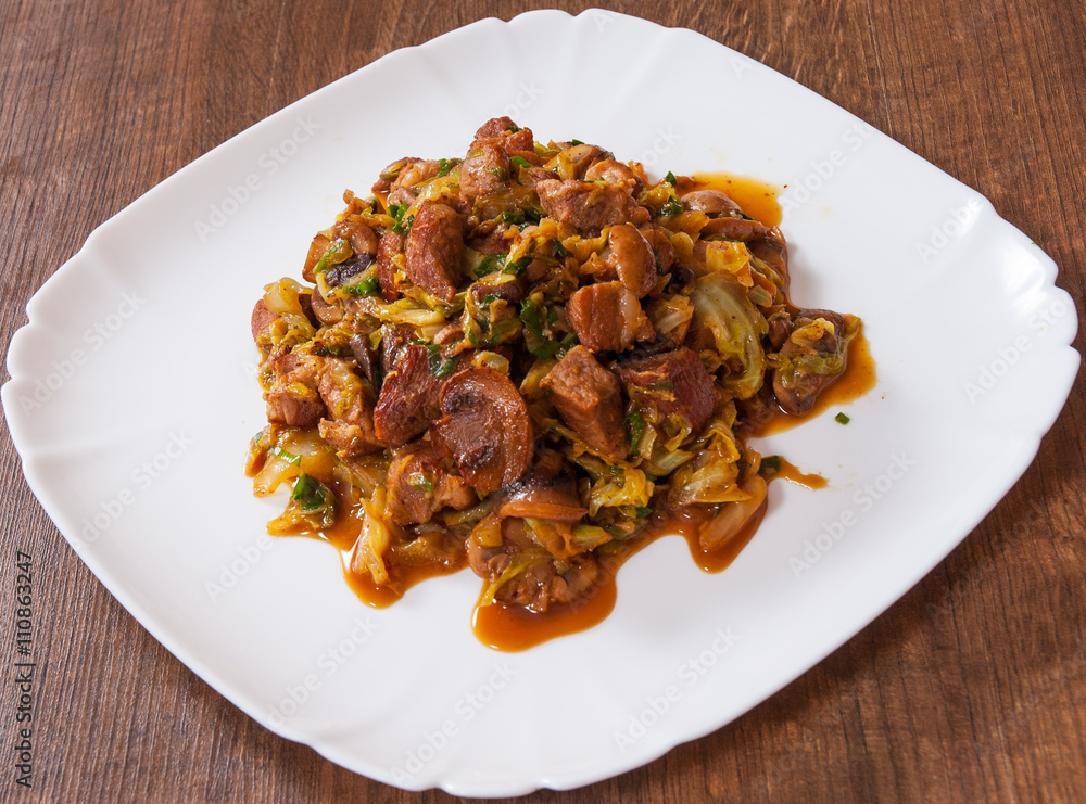 Stewed cabbage with mushrooms and meat in a plate on wooden table