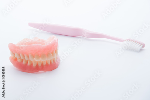 Acrylic dentures with toothbrush on white background.
