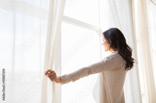 close up of pregnant woman opening window curtains